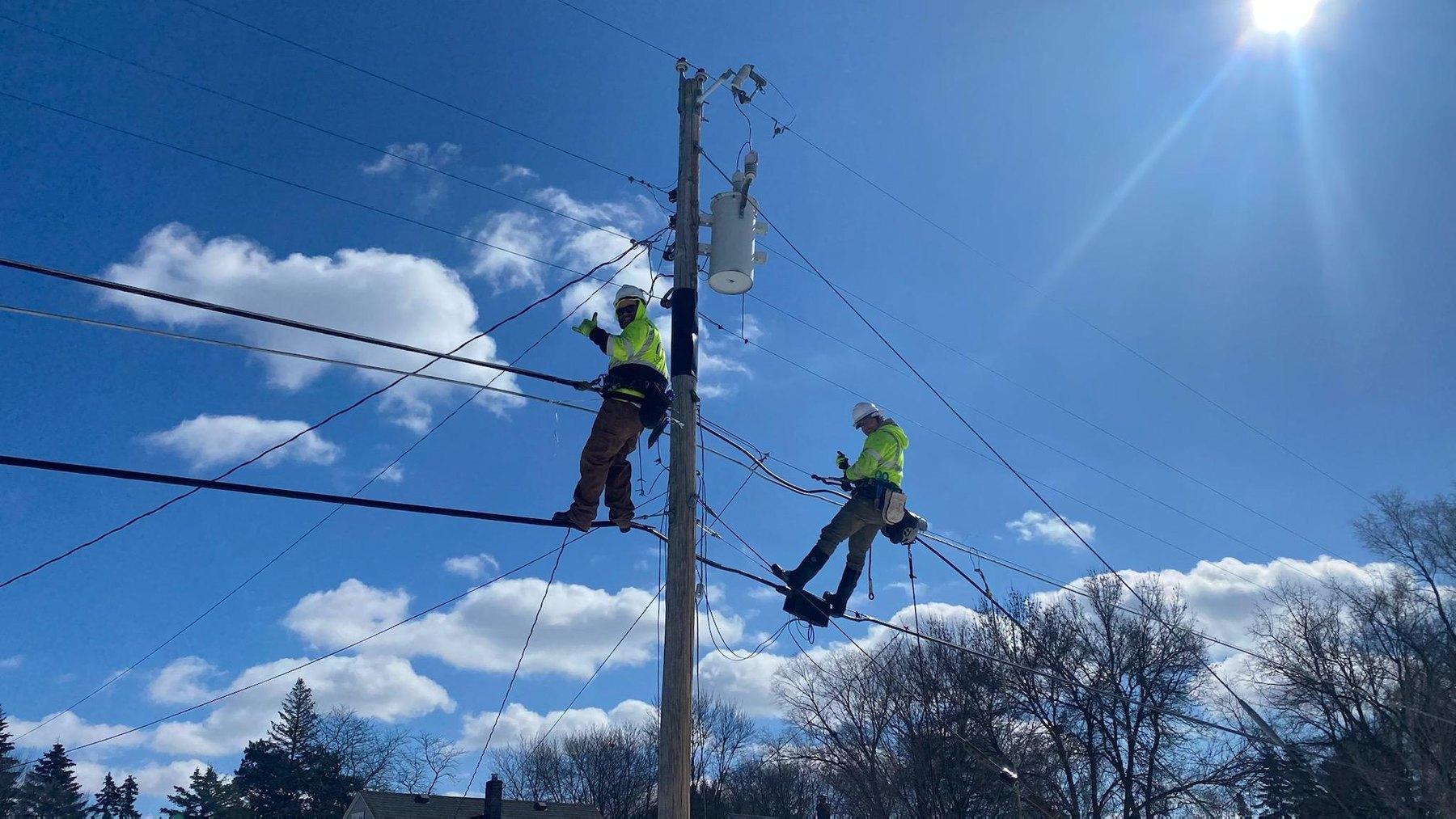 Two MCI linemen working from the strand on a joint-use pole against a blue sky